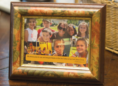 A handmade volunteer appreciation gift of a picture frame sits on a desk. In the frame is a collage of pictures and a Bible verse.