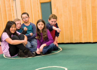 A group of five children huddled in a tabled circle on the ground.