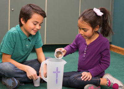 Two elementary-aged children putting stones in a pitcher for a Bible activity.