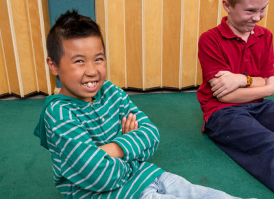An elementary aged boy smiles with his hands across his chest.