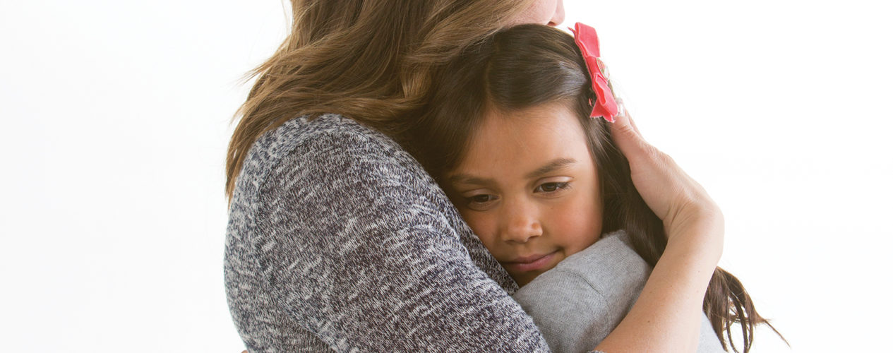 A woman volunteer embraces and elementary aged girl in a large hug.
