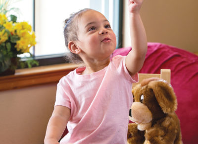 A toddler girl smiles as she points upwards.