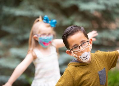 Two children playing outside wearing masks.