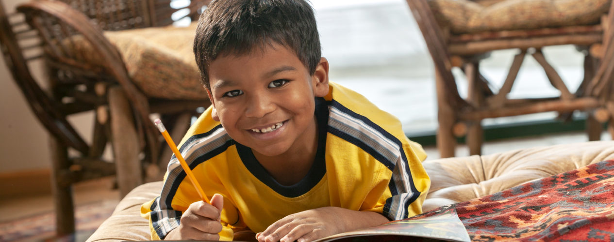 boy smiling while writing in book