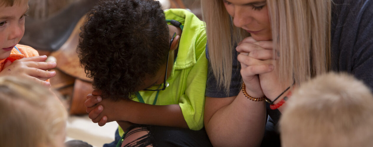 A female leaders prayers with a group of children at Vacation Bible School