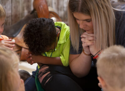 A female leaders prayers with a group of children at Vacation Bible School