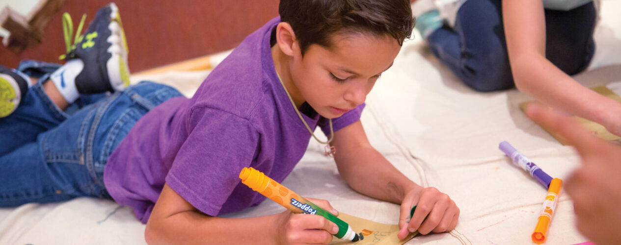 Boy writing on a piece of paper using markers.