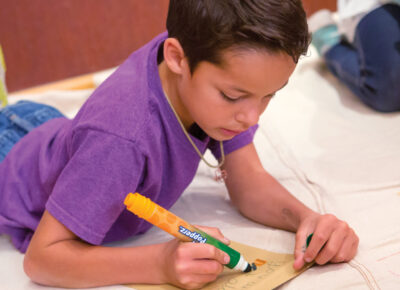 Boy writing on a piece of paper using markers.