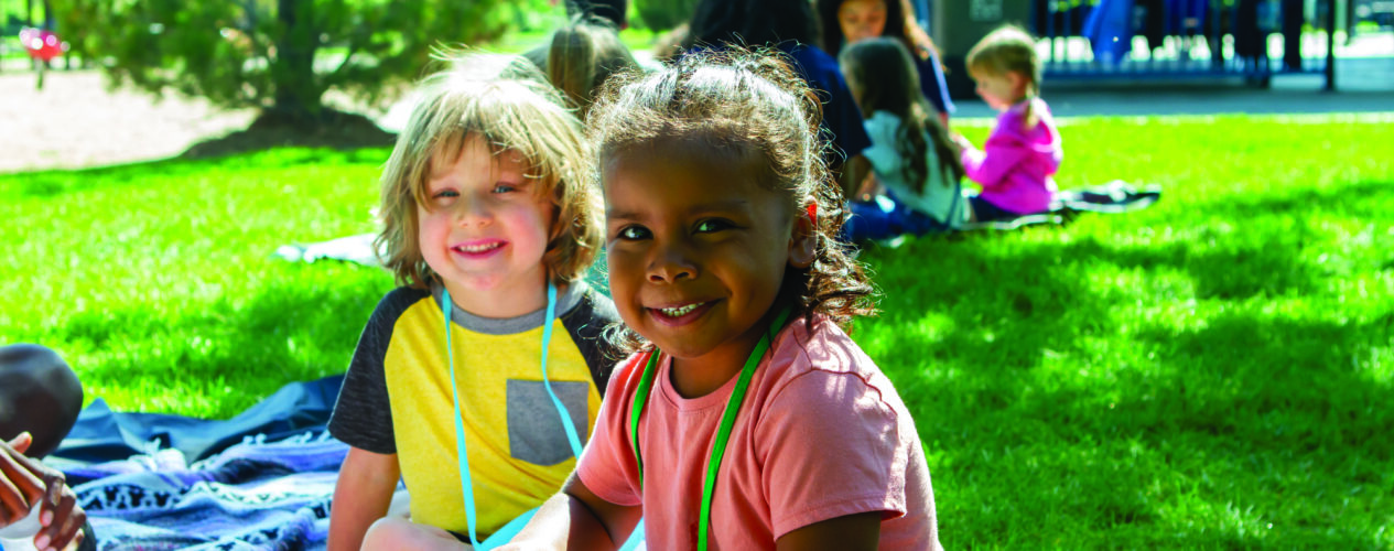 Kids smiling at the camera as they sit on a picnic blanket at their church outreach