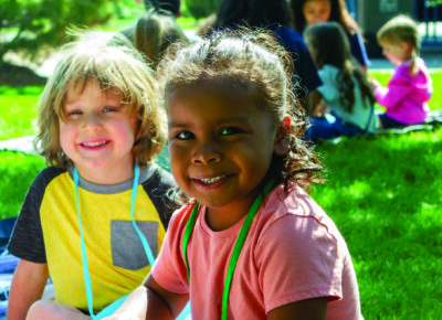 Kids smiling at the camera as they sit on a picnic blanket at their church outreach
