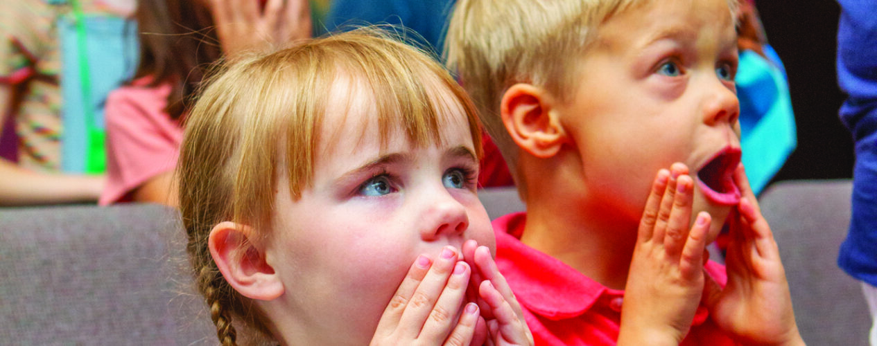 kids in a children's ministry setting with their hands by their mouths.