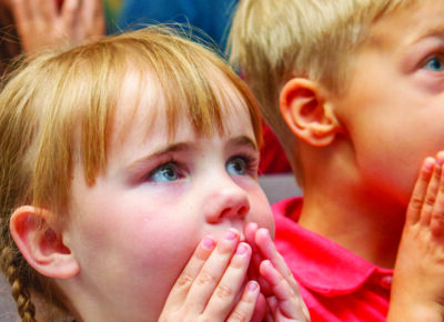 kids in a children's ministry setting with their hands by their mouths.