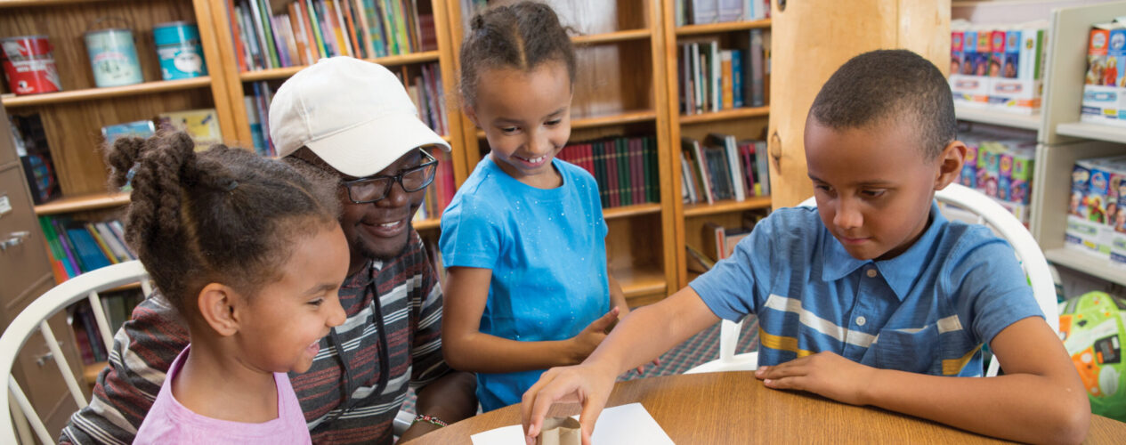 kids and children's ministry leader in a small church setting gathered around a table working on an object lesson.