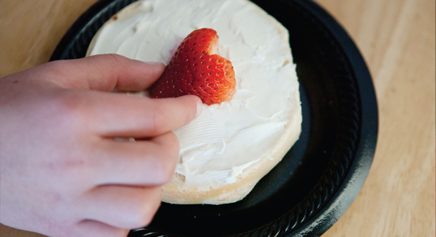 A bagel topped with cream cheese and a half of a strawberry.